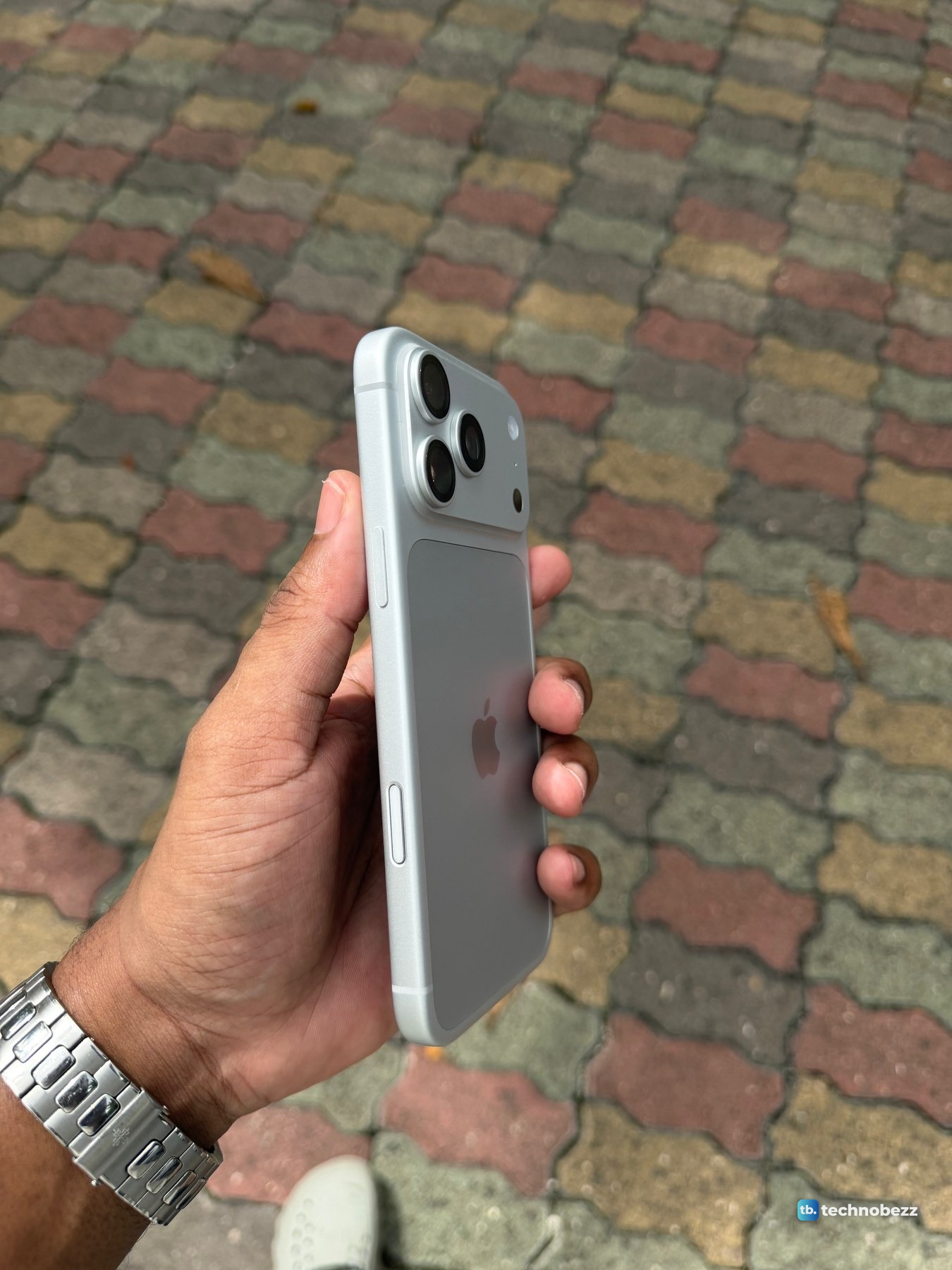 iPhone 18 Pro Max held side on over colored paving, showing the edge, the buttons and the raised camera bar