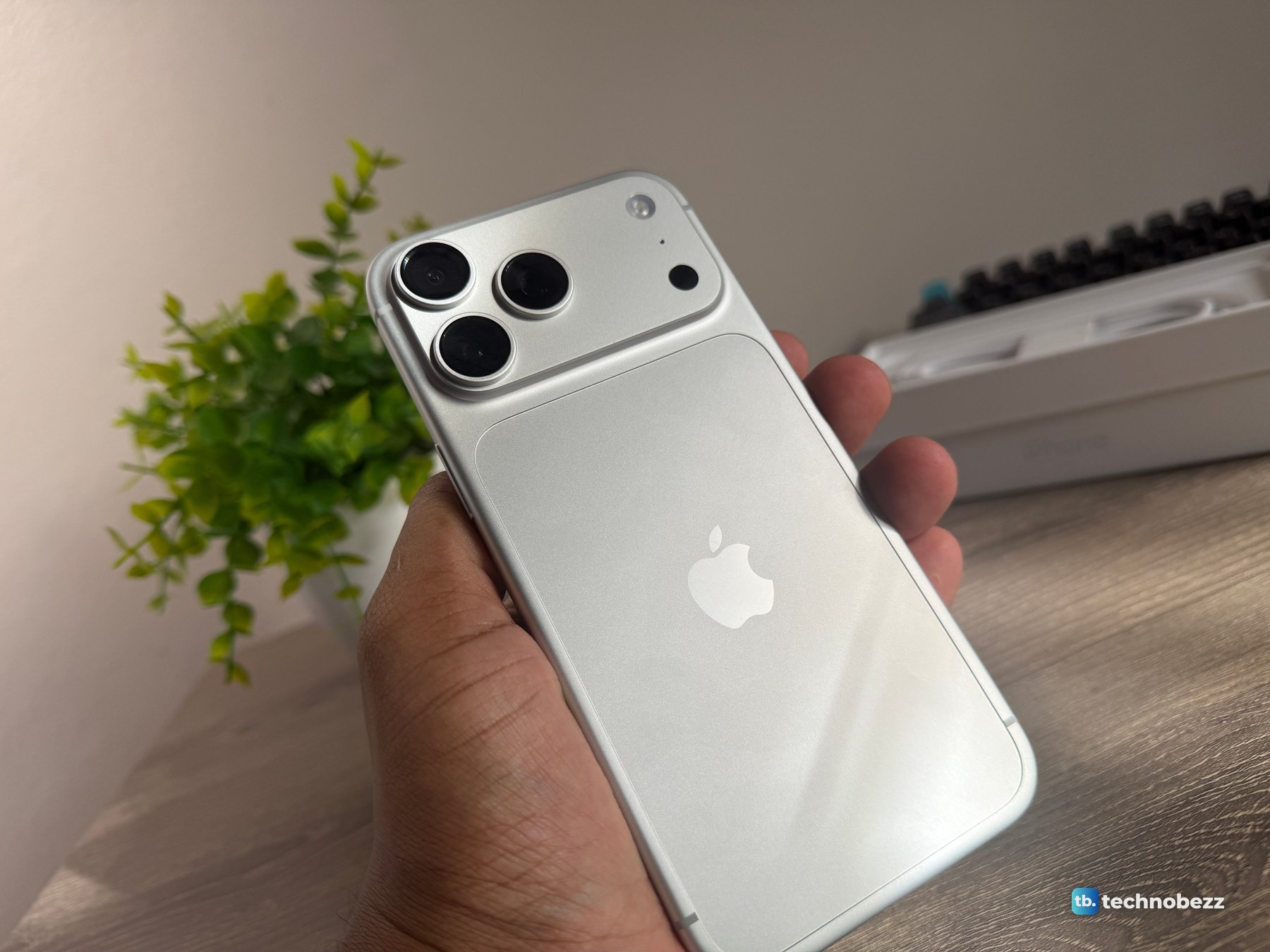 Back of the silver iPhone 18 Pro Max held in one hand at a desk, with the camera bar at the top