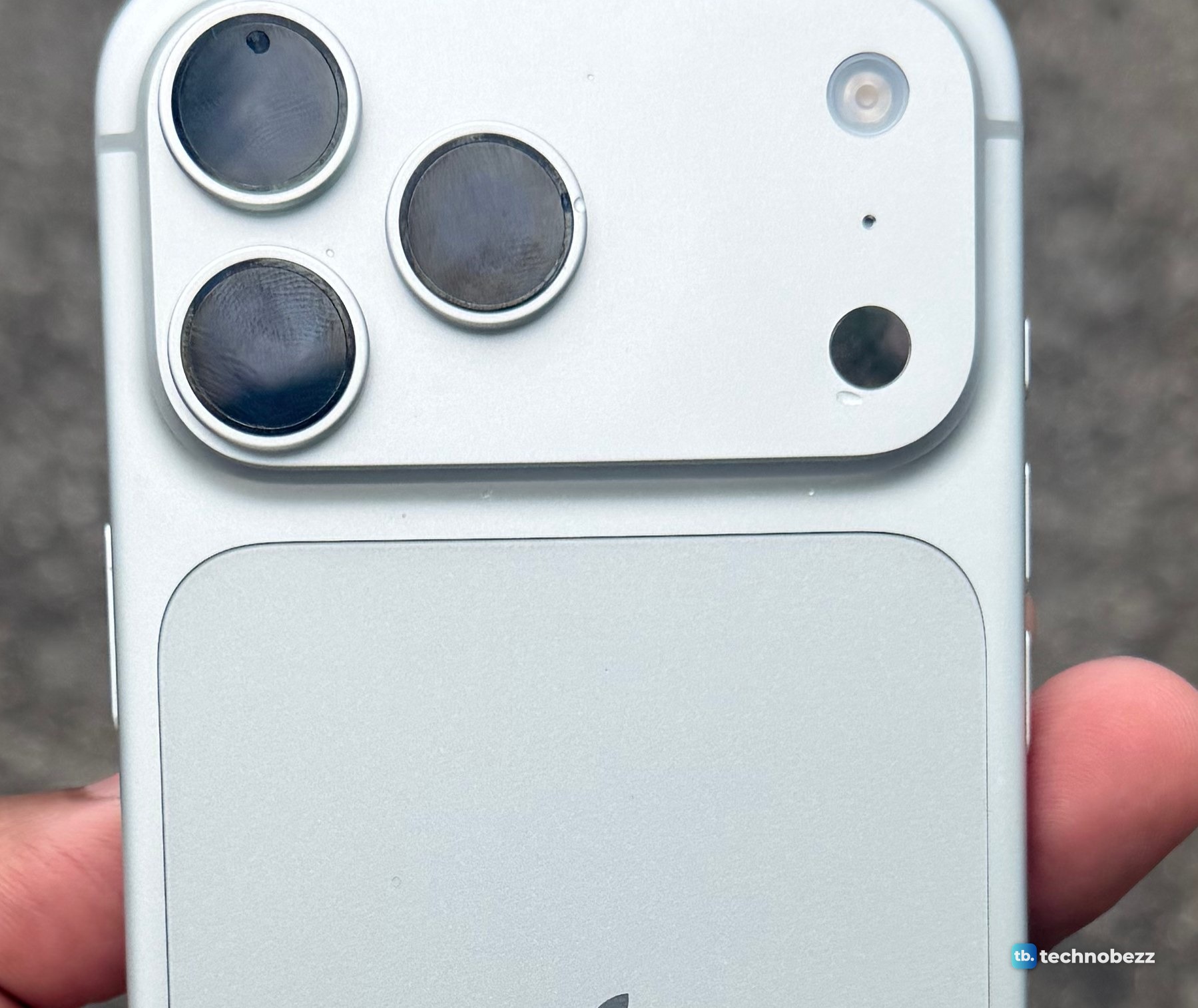 Close-up of the silver iPhone 18 Pro Max camera bar with fingerprints visible on the three black lenses and a clean silver back