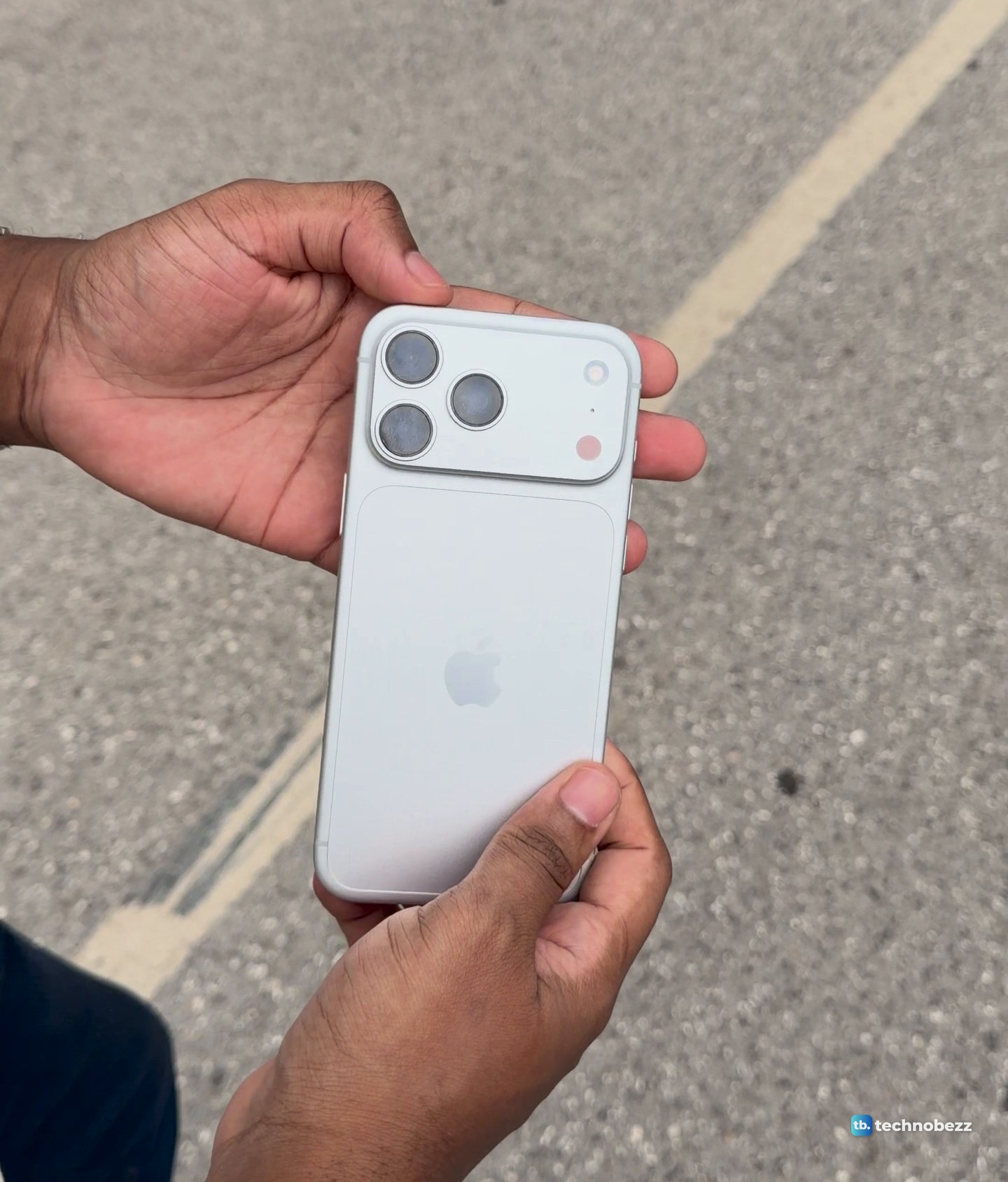 The back of the iPhone 18 Pro Max held between two hands over asphalt