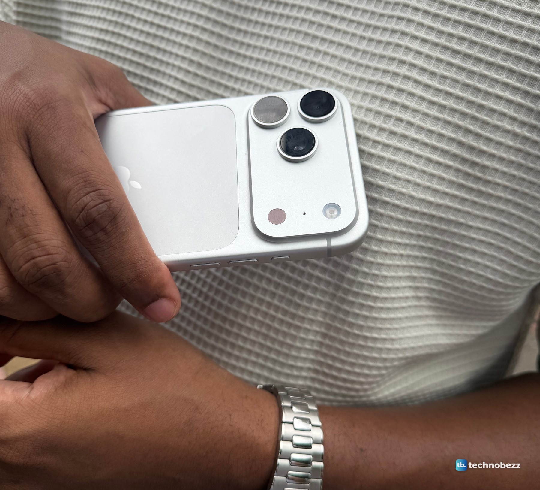 A close view of the iPhone 18 Pro Max camera bar with three lenses, the flash and a sensor, held sideways against a cream shirt