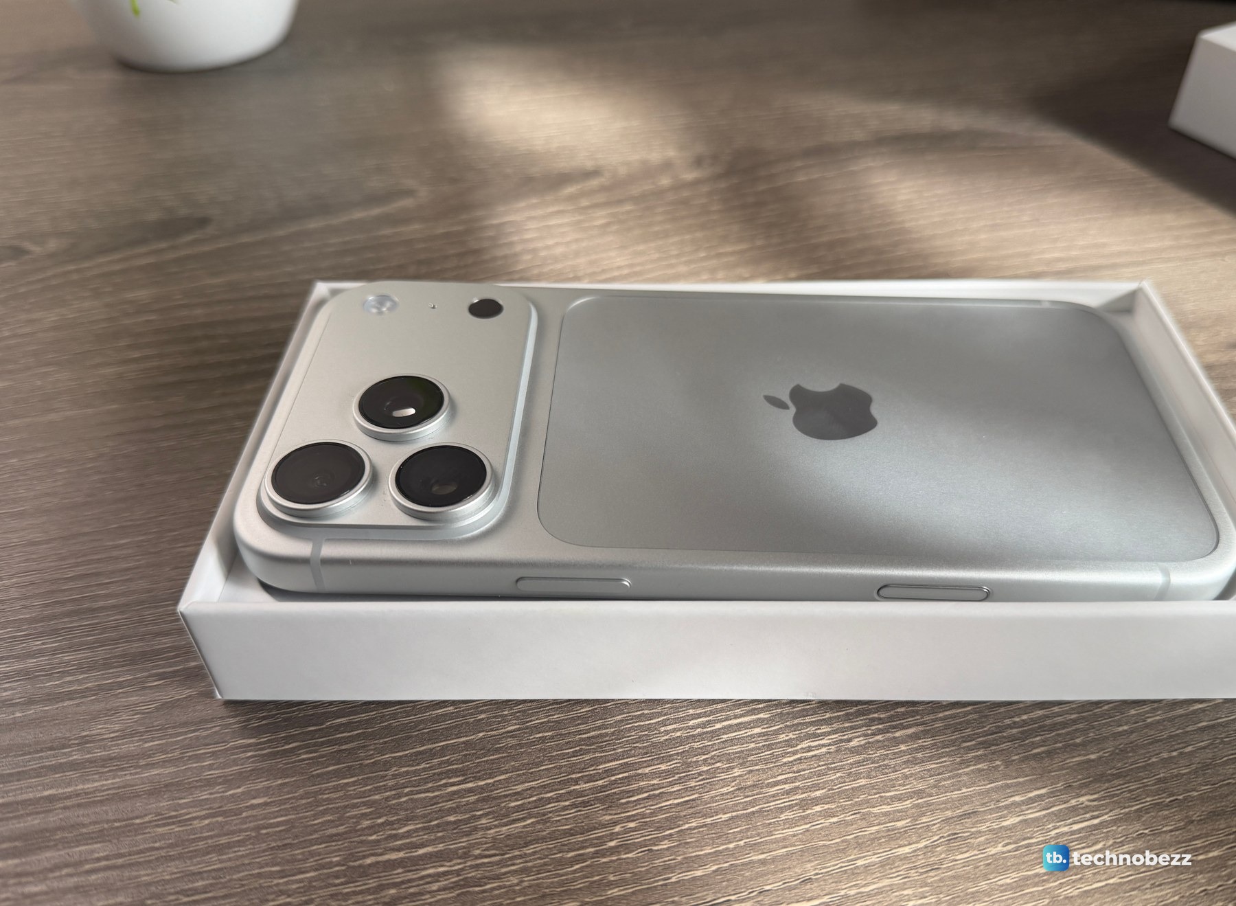 The iPhone 18 Pro Max lying face down in its white box tray, seen from a low angle with the camera bar nearest the lens