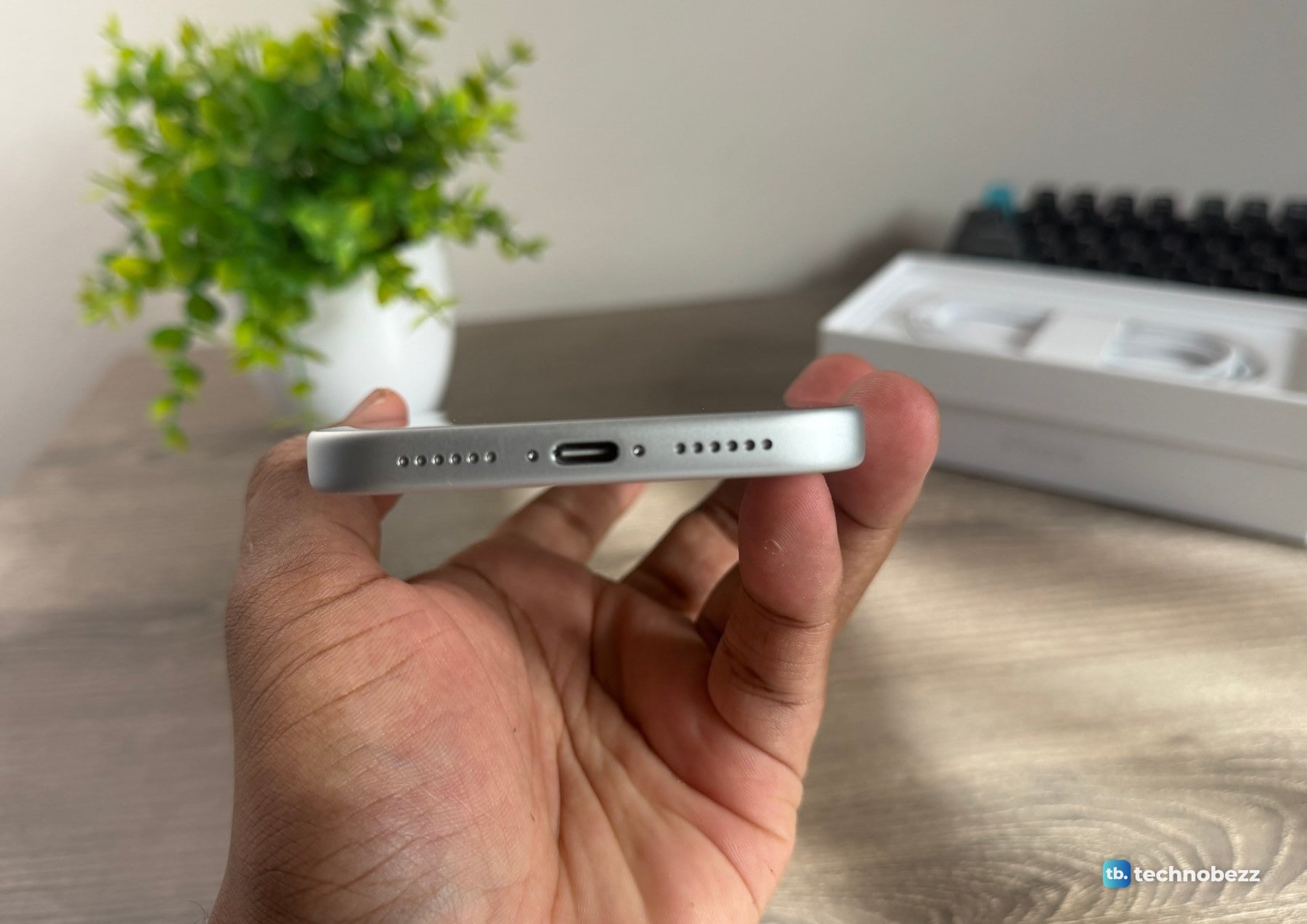 Bottom edge of the silver iPhone 18 Pro Max held in a hand, showing the USB-C port and a row of holes on each side