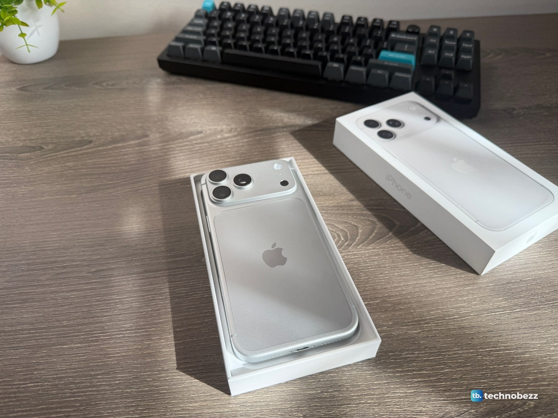 Silver iPhone 18 Pro Max face down in the box tray with the box lid lying beside it on a wooden desk