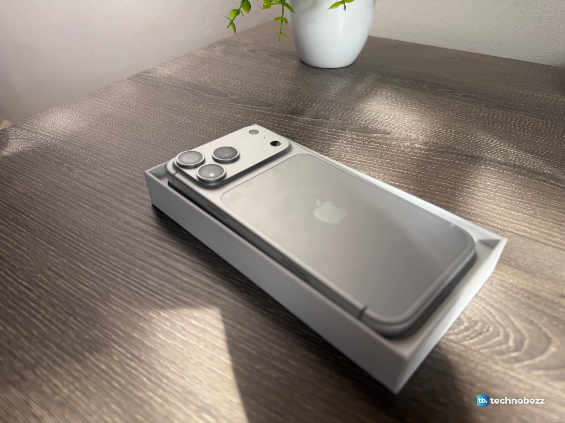 iPhone 18 Pro Max in its tray photographed from a low angle, the silver back looking dark gray
